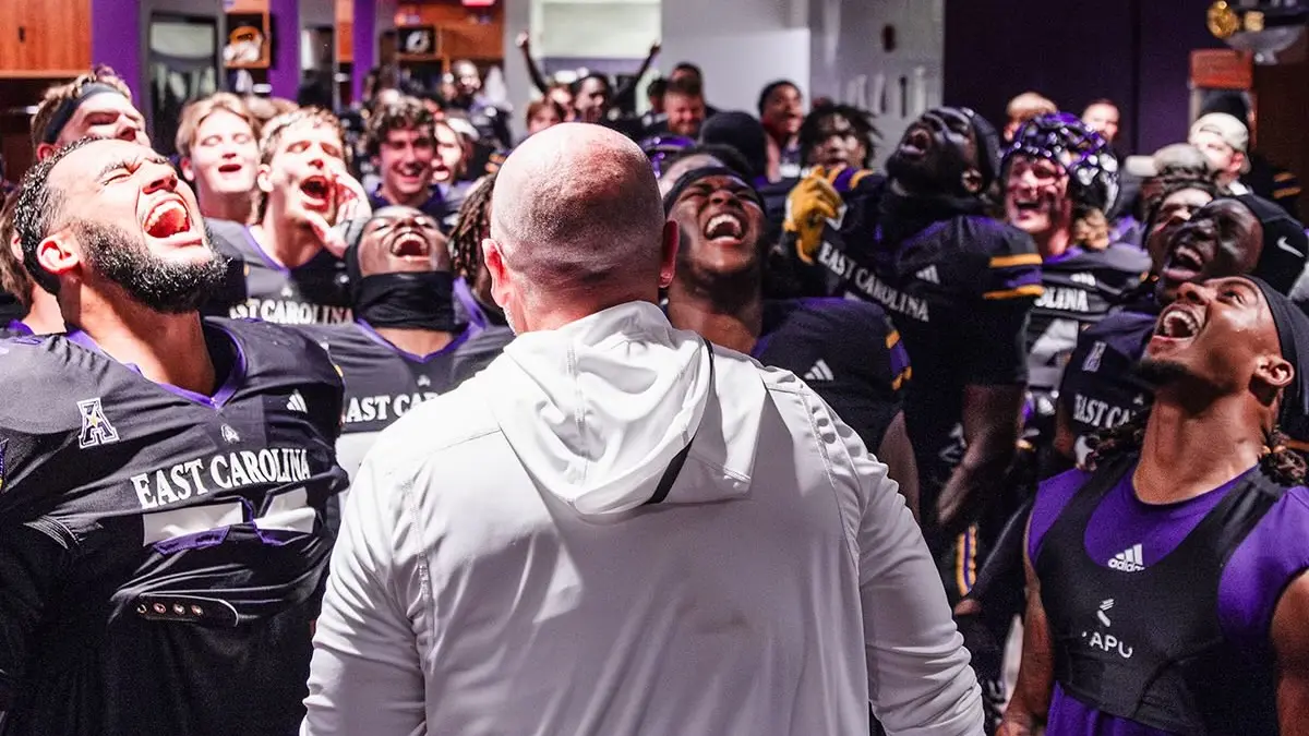 East Carolina football players and coach Blake Harrell celebrate in the locker room after their 2024 Night of the Boneyard win.