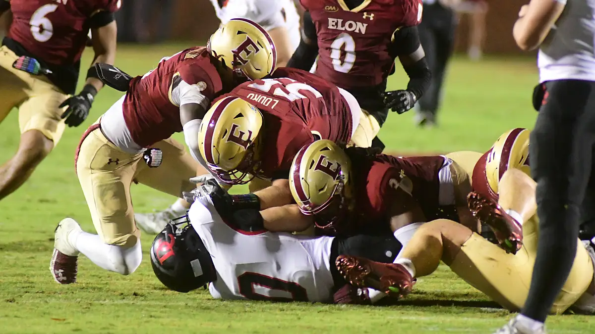 Elon football players pile on a Davidson ball-carrier in a night game at Rhodes Stadium in September 2025.