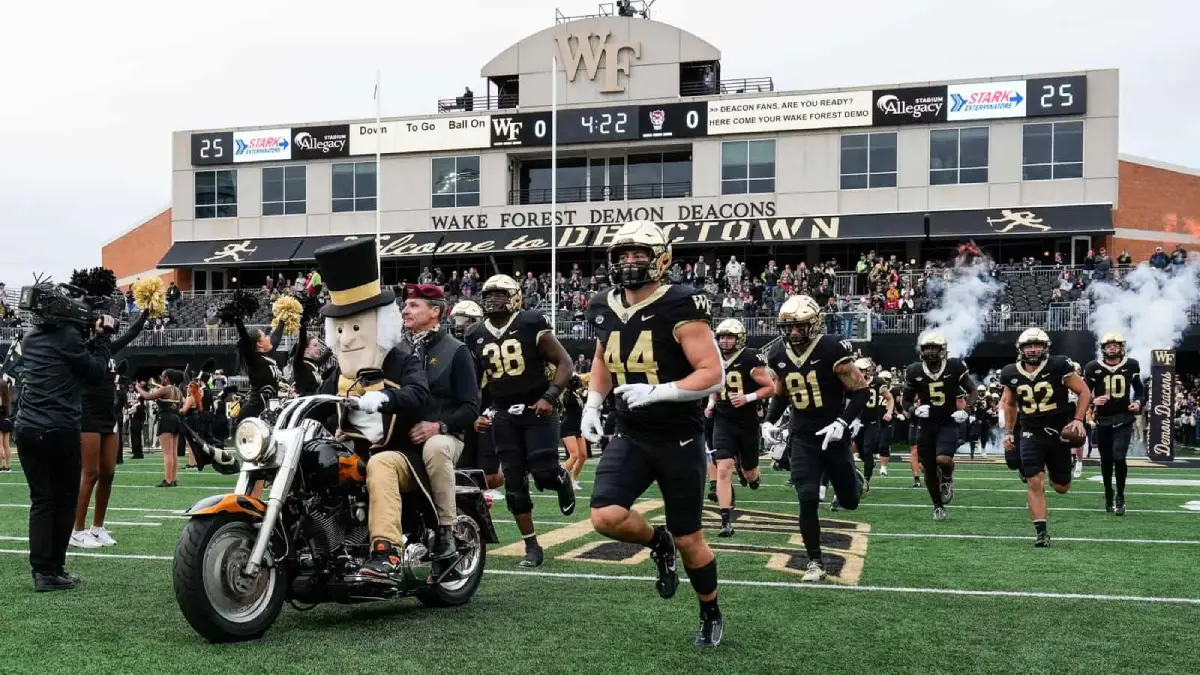 Wake Forest football players charge onto the field, accompanied by the mascot on a motorcycle, before a game.