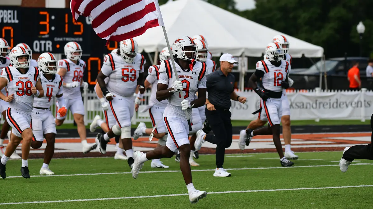 Campbell football players charge onto the field before a game against Western Carolina, with one player carrying an American flag